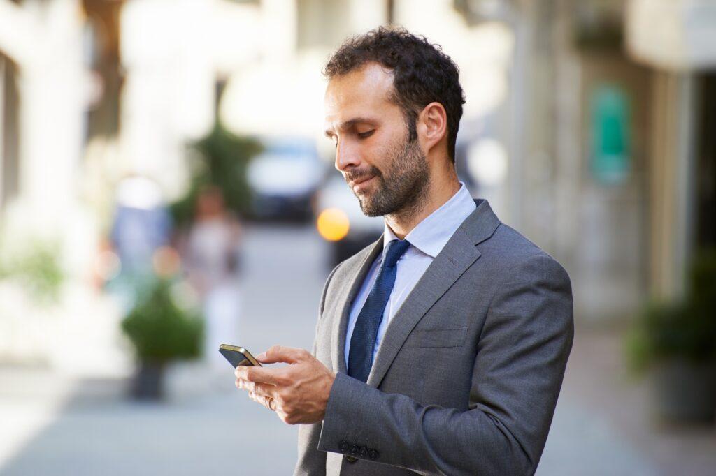 Business Man Typing Sms On Mobile Phone In Street