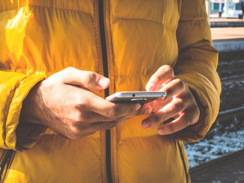 Hands using a mobile phone while wearing a yellow coat