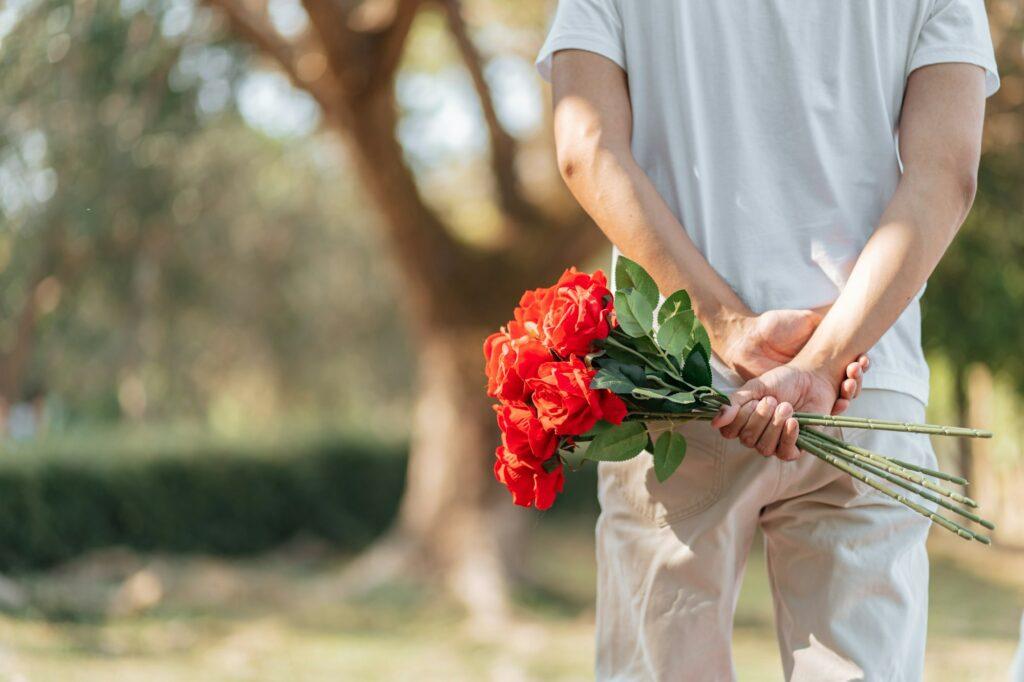 Happy romantic couple in Valentine's Day asian man hiding red rose flower behind
