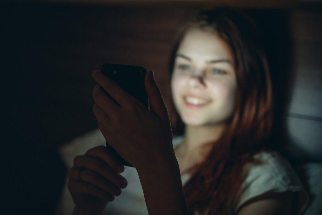 pretty woman lying in bed with phone in hand at night rest before bedtime