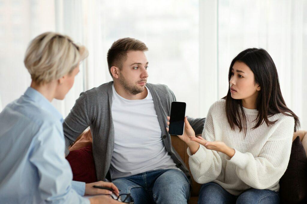 Wife Showing Cheating Husband's Cellphone During Therapy Session In Office