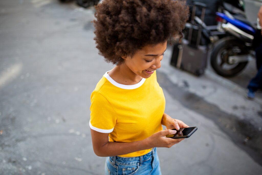 young black woman walking while using mobile phone in city